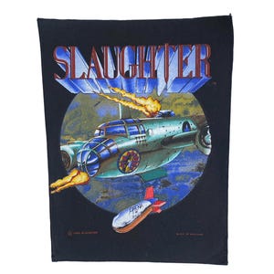 May include: A black fabric patch featuring the word SLAUGHTER in red and blue letters. A green aircraft with flames is depicted inside a circle, with a smaller bomb-shaped object labeled ARENA OF BUGS flying below it against a blue background.