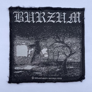 May include: A square black and white woven fabric patch featuring the text BURZUM in a gothic font at the top. The central graphic depicts a dark landscape with a silhouetted figure and a tree. The text MISANTHROPY RECORDS 2003 is at the bottom.