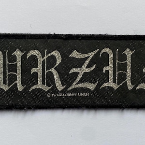 May include: Black rectangular patch with the word "BURZUM" in silver gothic lettering. The text "©1997 MISANTHROPY RECORDS" is printed below the main text. The patch has a black border.