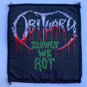 Op de afbeelding: Een vierkante zwarte stoffen patch met het geborduurde bandlogo OBITUARY in lichtpaars met rode druipende accenten. Onder het logo is de tekst SLOWLY WE ROT geborduurd in felgroen. De tekst BLUE GRAPE MERCHANDISING staat onderaan.