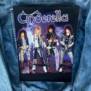 May include: A denim jacket with a large, rectangular patch featuring the band Cinderella. The patch shows four band members in colorful stage attire, with the band's name in a stylized font at the top. The jacket is a light blue wash.