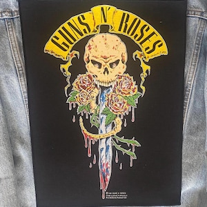May include: Black patch with the Guns N' Roses logo, a skull, roses, and a dagger. The logo is yellow, the skull is beige, the roses are red and yellow, and the dagger has a blue and red design.