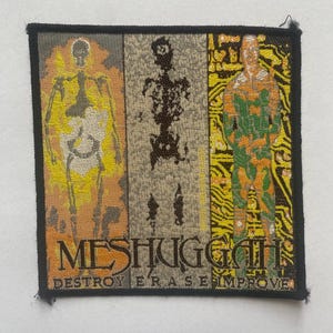 Op de afbeelding: Geborduurde vierkante patch met een zwarte rand. Het heeft drie verticale panelen met menselijke figuren in skelet- en printplaatstijl. De bandnaam "MESHUGGAH" en de zin "DESTROY ERASE IMPROVE" staan onderaan.