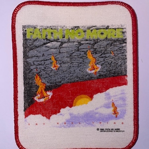 Puede incluir: Un parche rectangular con borde rojo presenta el texto "FAITH NO MORE" en letras verdes sobre un gráfico de un paisaje rojo y gris con llamas naranjas. El parche es blanco con borde rojo.