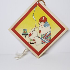 May include: A vintage diamond-shaped card with a red border and a yellow background. A woman in a red hat and fur coat sits with a cigarette and a lamp in the background.