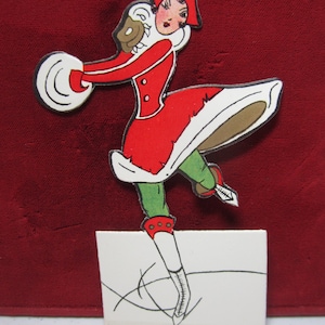 May include: A vintage-style illustration of a woman ice skating, dressed in a red coat with white trim and a matching hat. The figure is set against a deep red background, with green leggings and white ice skates.