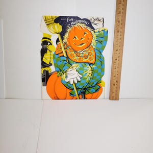 May include: A vintage Halloween scarecrow cutout featuring a pumpkin head, a blue and green checkered shirt, and a black crow. The text reads "Have fun on Halloween!". A wooden ruler next to the cutout shows it is approximately 12 inches tall.