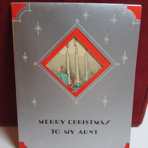 May include: Vintage Christmas card with a silver background and red accents. The card features a diamond-shaped window with an illustration of lit candles. The text "MERRY CHRISTMAS TO MY AUNT" is printed below the window.