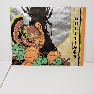May include: A vintage Thanksgiving greeting card with a silver background featuring a brown and orange turkey with a green and orange pumpkin in the foreground. The card has the word "GREETINGS" written vertically on the right side.