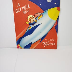 May include: A vintage get well card featuring a retro illustration of a child in a rocket ship. The card has a red and blue background with the text "A Get Well Wish" and "To a Young Space Traveler."