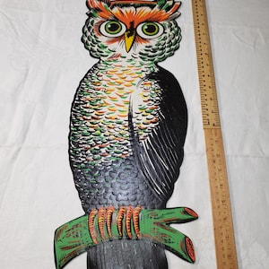 May include: A flat, die-cut owl wall decoration featuring black, green, and orange colors, perched on a green branch. A wooden ruler placed vertically next to the owl shows a height of approximately 10 inches, while a horizontal ruler shows a width of 4 inches.
