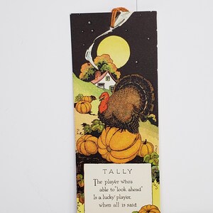 May include: A rectangular bookmark featuring a Thanksgiving illustration of a turkey perched on a large pumpkin. The scene includes a house, a full moon, and smaller pumpkins. Text reads: TALLY The player who's able to look ahead Is a lucky player, when all is said.