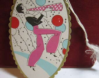 May include: A vintage oval-shaped paper tag with a gold border and scalloped edges. The tag features a colorful illustration of a person playing a trumpet with pink pants and a black and white patterned shirt. The background is white with black and white confetti and blue and red balloons.