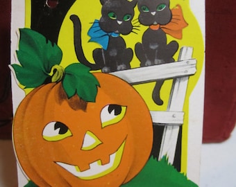 May include: A vintage Halloween card featuring a smiling jack-o'-lantern pumpkin with two black cats wearing blue and orange bows sitting on a fence in front of a yellow moon.