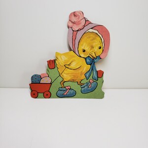 May include: A yellow chick wearing a pink bonnet and blue shoes pulls a red wagon filled with colorful Easter eggs.
