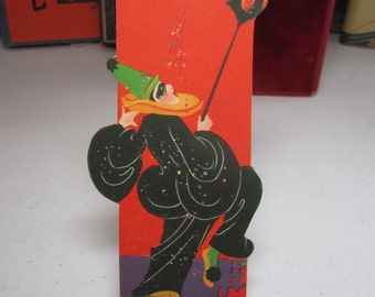 Colorful unused art deco 1920&#39;s-30&#39;s die cut mardi gras costume ball bridge tally man in clown costume and black mask holds lantern confetti