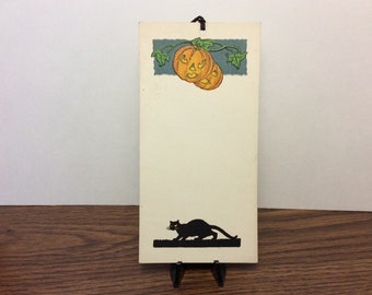 1920's-30's unused halloween bridge tally card black cat with yellow eyes creeping under 2 scary looking Jack O’Lanterns and vines