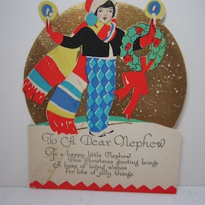 May include: A vintage Christmas card featuring a girl in a blue and white patterned dress and a red scarf holding a wreath and candles. The card has a gold background with a snowy effect and the text "To A Dear Nephew" and a poem.