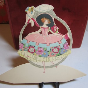 Adorable 1920&#39;s unused die cut place card large engagement ring with pretty girl in elaborate dress inside cupid sitting at the top of ring