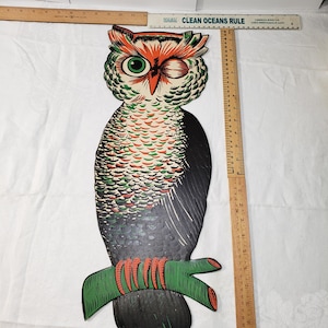 May include: A flat, die-cut owl wall decoration featuring a winking expression, green and orange plumage, and black wings. The owl is perched on a green branch. A wooden ruler placed alongside shows the owl measures approximately 12 inches in height.