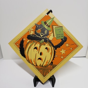 May include: A vintage Halloween card featuring a black cat wearing a witch's hat and holding a book that says "BLACK MAGIC BY I OWL". The cat is sitting on top of a jack-o'-lantern with a sad face. The background is orange with white stars.