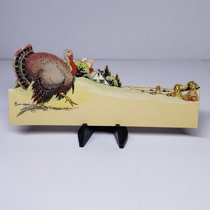 May include: A vintage Thanksgiving place card featuring a colorful illustration of a turkey walking towards a farmhouse with a field of pumpkins in the background.
