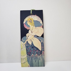 May include: A rectangular bookmark featuring an Art Nouveau illustration of a woman in a flowing gown and a parasol. The woman is depicted in profile with blonde hair, set against a dark blue background. The gown is in shades of blue, cream, and green.