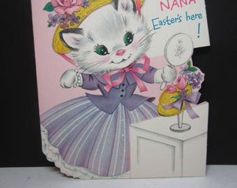 1960’s colorful die cut glitter Norcross easter card for Nana ,darling white kitten dressed in purple dress trying on bonnet looks inmirror