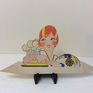 May include: A vintage birthday card featuring a woman with red hair and a pink and yellow cake with lit candles.