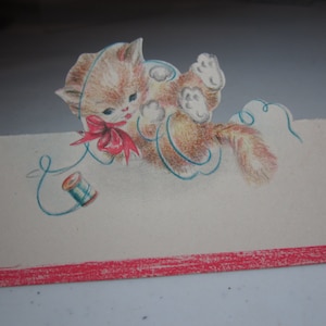 May include: A vintage place card with a cute cartoon kitten holding a spool of thread. The kitten is wearing a red bow and is surrounded by a blue swirl. The card has a red stripe at the bottom.