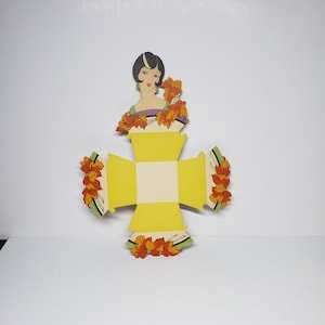 May include: A yellow, die-cut box with a vintage illustration of a woman with a bob haircut and autumn leaves. The box is decorated with orange and yellow fall leaves. The box is open and ready to be assembled.