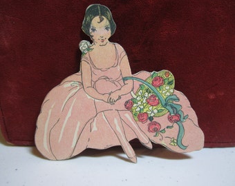 1920's-1930's die cut art deco place card pretty flapper girl in pink dress holding a basket of red roses unused