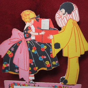 1920's art deco die cut unused novelty place card young girl in fancy party dress and a pierrot clown holds box with tiny answer to riddle