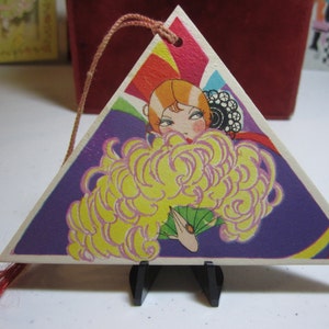 May include: A triangular card with a colorful design featuring a woman with a large yellow feather boa and a fan. The card has a red tassel attached to it.