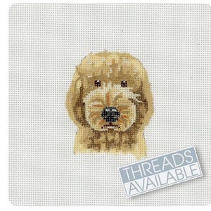 Peut inclure: Une toile de point de croix représentant le visage d'un chien golden doodle. Le chien a un pelage brun clair et duveteux, des yeux foncés et un nez noir. Le texte "THREADS AVAILABLE" est dans un rectangle bleu en bas à droite.