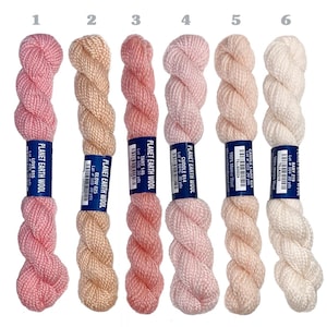 May include: Six skeins of Planet Earth Wool yarn in various shades of pink, peach, and cream. Each skein has a label with the yarn name and lot number. The yarn is labeled as 100% Merino Wool.