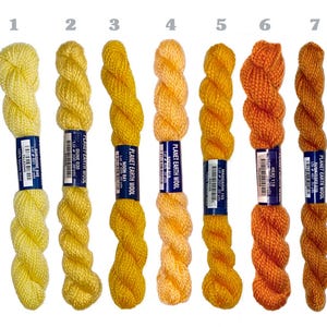 May include: Seven skeins of Planet Earth Wool yarn arranged vertically and numbered one through seven. The colors range from pale yellow to deep orange and brown. Each skein features a blue label with white text detailing the specific color name.