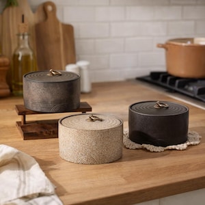 May include: A set of three ceramic mugs with a speckled, matte finish. The mugs are in shades of cream, light gray, and dark gray. Each mug has a simple, modern design and a rounded handle.