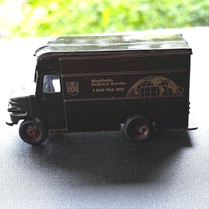 May include: A dark brown toy delivery truck featuring the UPS logo, the text Worldwide Delivery Service, and 1 800 Pick UPS. The vehicle has a globe graphic on the side, a small driver cabin window, and four dark wheels with reddish-brown rims.