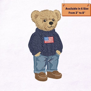 May include: Embroidered teddy bear wearing a navy blue cable-knit sweater with an American flag patch, blue jeans, and brown moccasins. The text on the sign says "Available in 6 Size From 2" to 8".