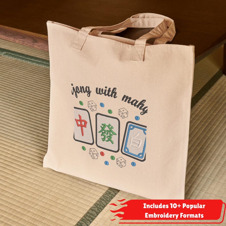 May include: A beige canvas tote bag with the words "jong with mahy" above a graphic of three Mahjong tiles and dice. The tiles are red, green, and blue. The bag has two handles and a red banner at the bottom.