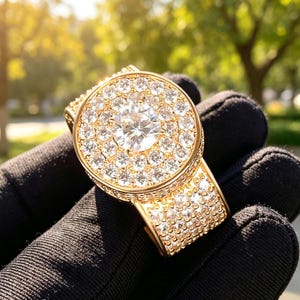 May include: A gold ring featuring a large, round, central clear gemstone surrounded by multiple smaller clear stones in a circular halo setting. The band is wide and fully encrusted with rows of small, sparkling clear stones throughout.