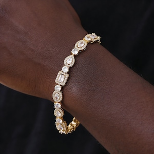 May include: A gold bracelet with a variety of clear gemstones. The bracelet features round, oval, pear, and square-cut stones set in gold. The bracelet is displayed against a dark background.