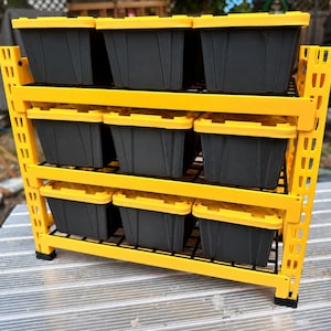 May include: A yellow metal storage rack with three horizontal shelves, each holding three black plastic storage bins with yellow lids. The rack features a grid-style shelf design and vertical support beams with rectangular cutouts for adjustment.