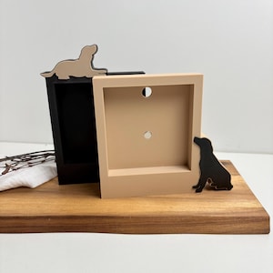 Könnte beinhalten: Zwei quadratische Holzpflanzgefäße, eines schwarz und eines beige, jeweils mit einer Hundesilhouette. Der beige Pflanztopf hat eine schwarze Hundesilhouette an der Seite, und der schwarze Pflanztopf hat eine beige Hundesilhouette oben. Die Pflanzgefäße stehen auf einer Holzoberfläche.