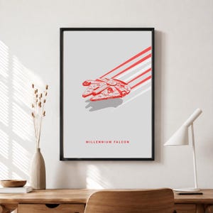 Könnte beinhalten: Ein gerahmter Kunstdruck mit einer roten Strichzeichnung des Raumschiffs Millennium Falcon auf hellgrauem Hintergrund. Das Raumschiff ist mit Bewegungslinien dargestellt, die dahinter verlaufen, und der Text MILLENNIUM FALCON steht darunter.