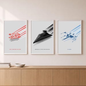 Könnte beinhalten: Ein Set aus drei gerahmten Wandbildern auf hellgrauem Hintergrund. Das linke Bild zeigt einen roten Millennium Falken, das mittlere einen schwarzen Imperialen Sternenzerstörer und das rechte einen blauen X-Wing, jeweils mit Bewegungslinien.