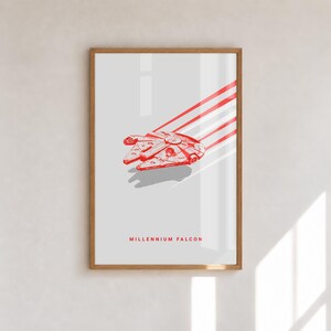 Könnte beinhalten: Ein gerahmter Kunstdruck mit einer roten Strichzeichnung des Raumschiffs Millennium Falcon auf hellgrauem Hintergrund. Das Schiff ist mit Bewegungslinien dargestellt, die dahinter verlaufen, und der Text MILLENNIUM FALCON ist darunter in Rot gedruckt.