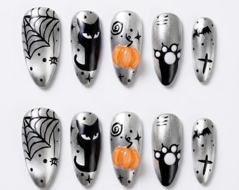 Può includere: Un set di dieci unghie finte a mandorla con base argento metallizzato. I disegni presentano ragnatele nere, la sagoma di un gatto nero, una zucca arancione, un'impronta di zampa nera, un pipistrello e una croce, decorati con piccoli puntini.