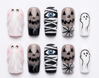 Può includere: Un set di dieci unghie finte con disegni di Halloween che includono fantasmi bianchi con guance rosa, zucche grigie con glitter neri, mummie con un occhio blu, zucche con ragnatele nere e fantasmi bianchi con contorni neri.